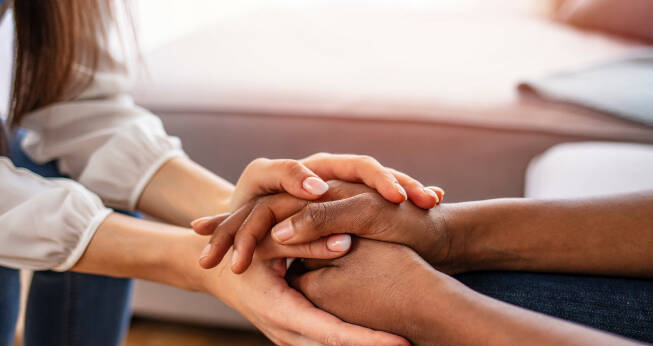 woman comforting a person by touching their hands