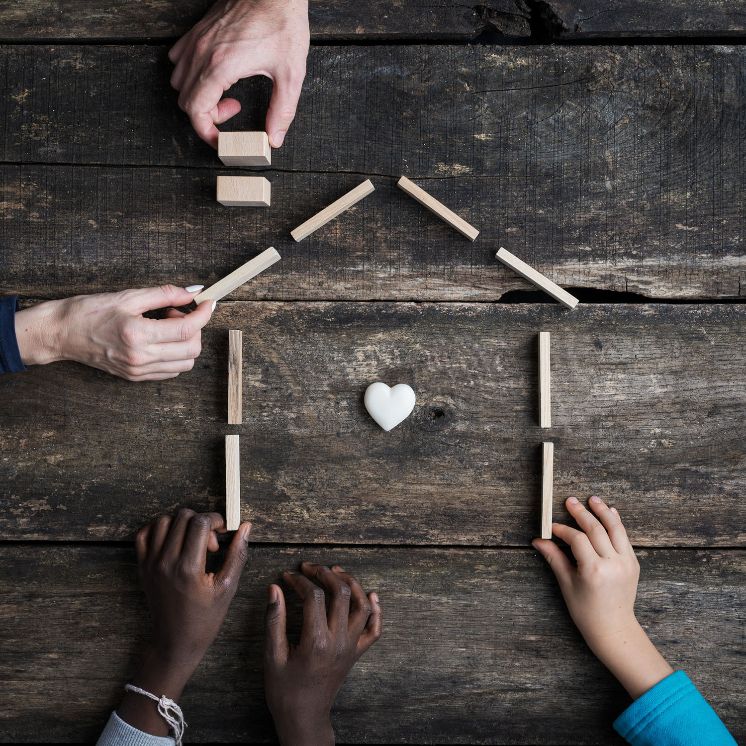 family of four constructing a small wooden home with a heart in the center