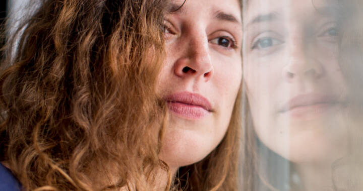 distressed woman looking out window - she looks like she's been crying