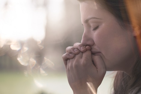Woman in distress folds hands with eyes closed